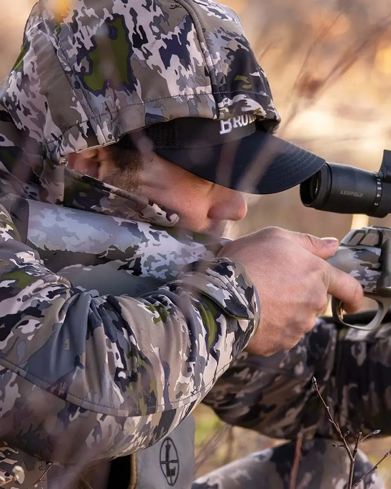 Hunter wearing OVIX camo aiming an X-Bolt rifle on a cliff