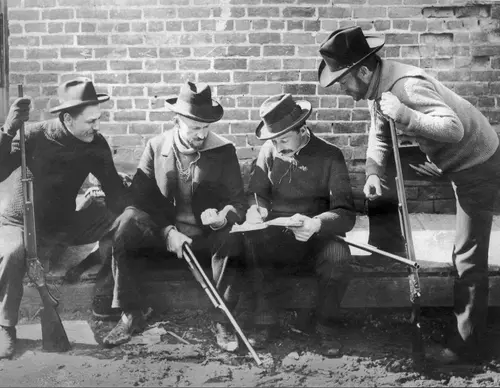 John M Browning shotgun in hand sitting on boardwalk with trap shooting team "4-Bs."